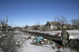A man pushes a bicycle along buildings damaged by fighting in the village of Nikishine